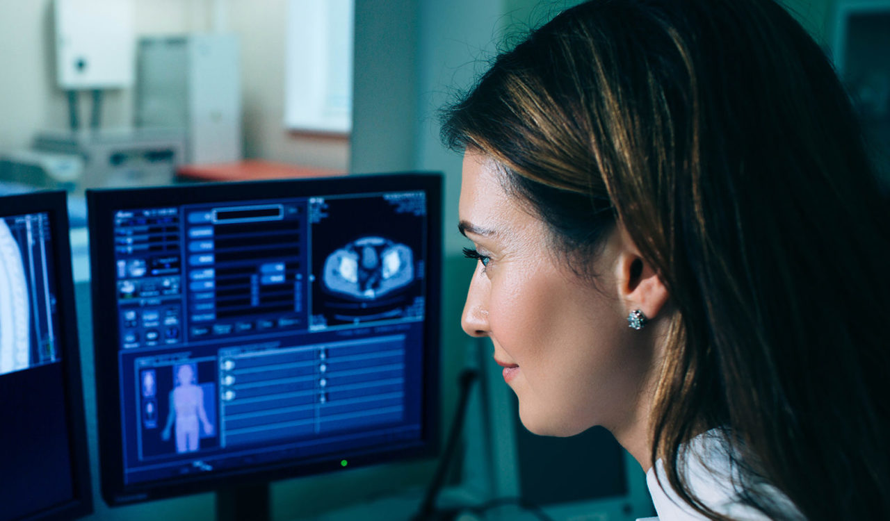 Radiologist reading a CT scan. Female doctor running CT scan from control room at hospital
